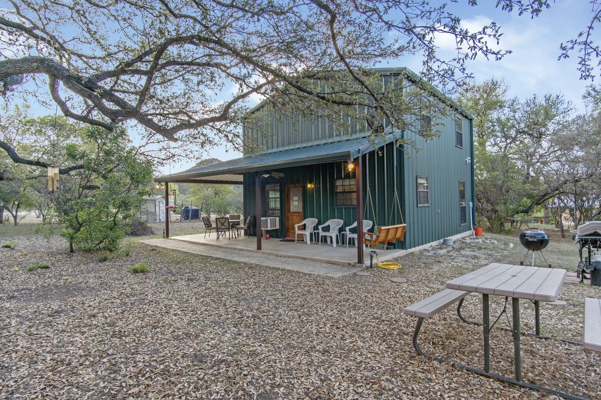 Cherry Creek Cabin &mdash; green metal cabin under live oaks with covered porch